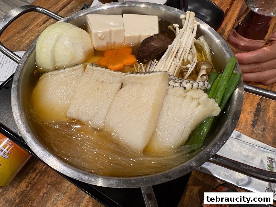 A steaming hot pot filled with fish, tofu, mushrooms, and vegetables.