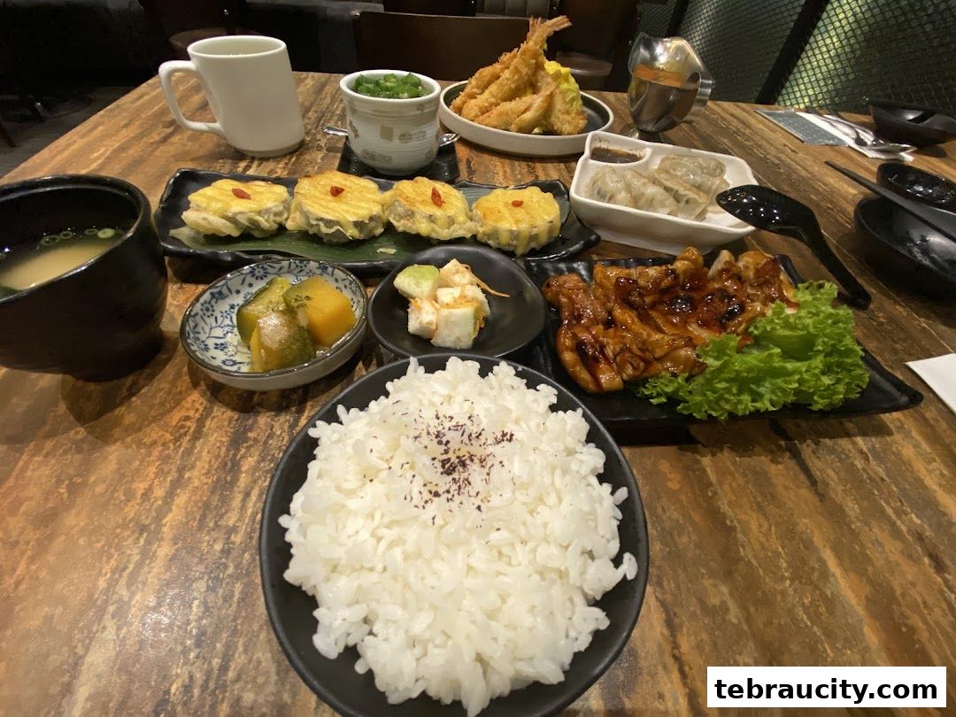 A table laden with a variety of Japanese dishes, including rice, teriyaki chicken, and tempura.