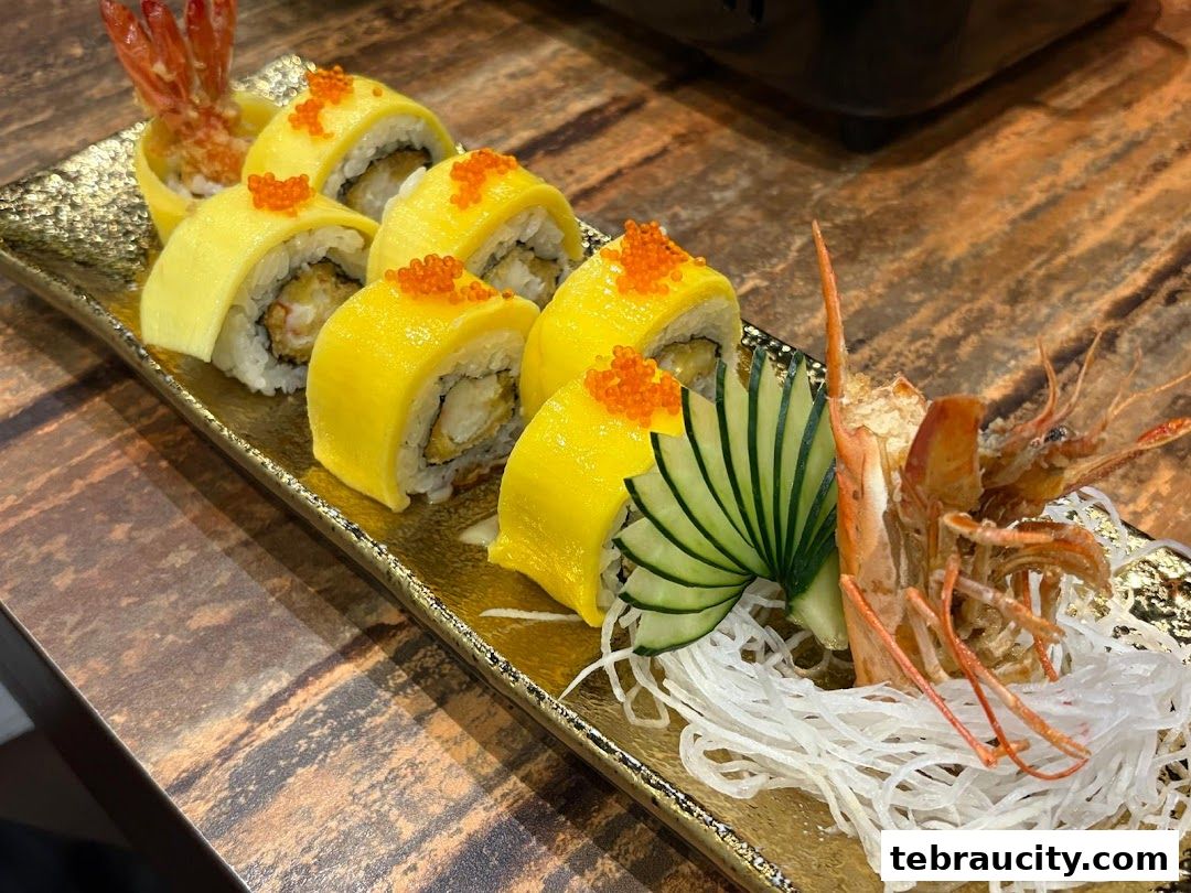 A close-up of a beautifully presented sushi roll with mango, tempura shrimp, and tobiko.