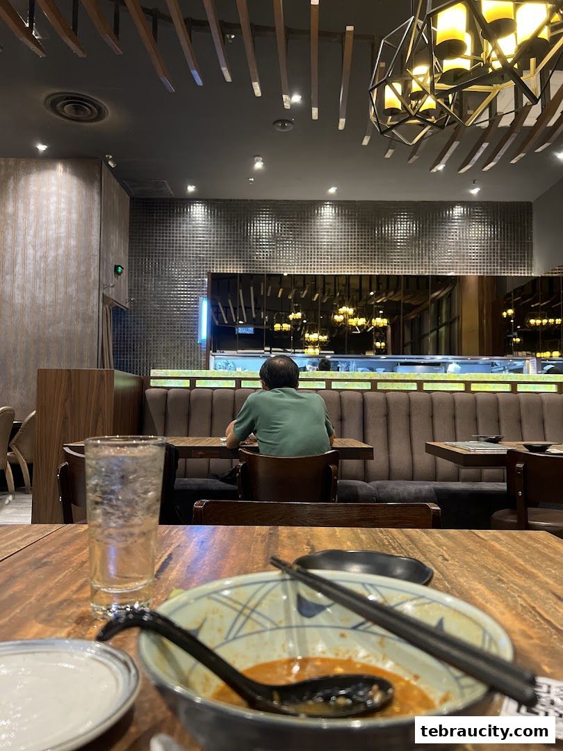 A person sits at a table in a Japanese restaurant with a bowl of food and a drink.