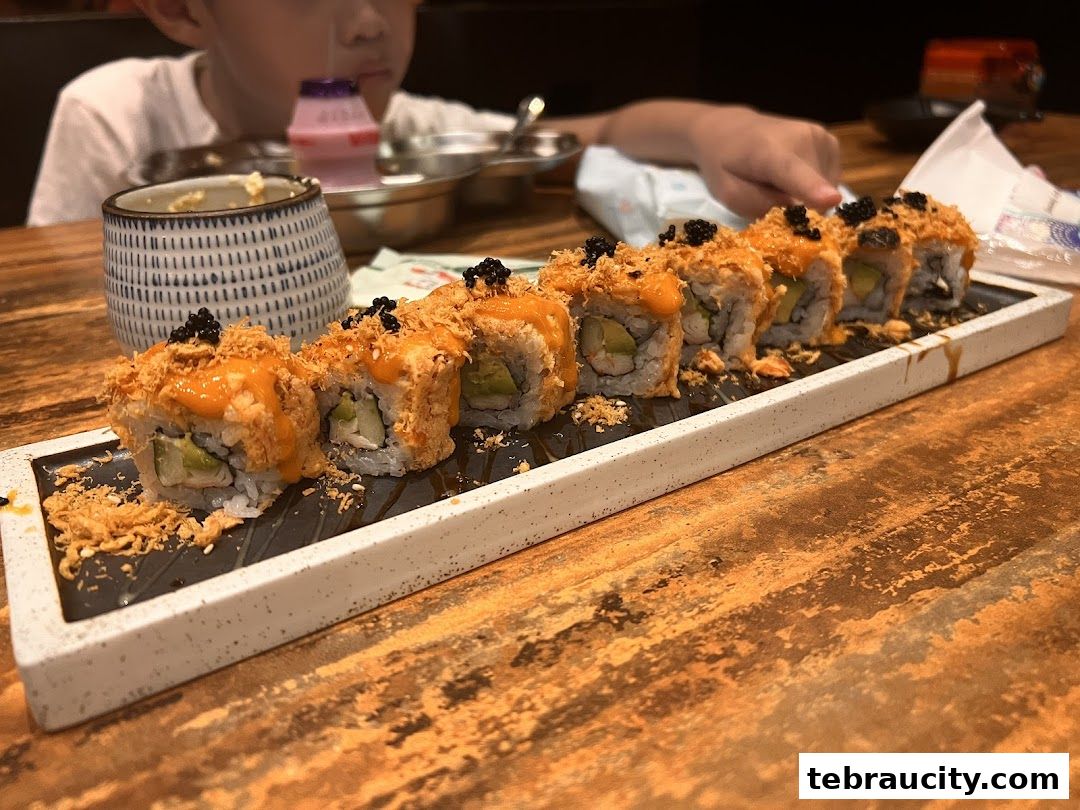 A plate of sushi rolls with sauce and toppings, served on a table with a child in the background.