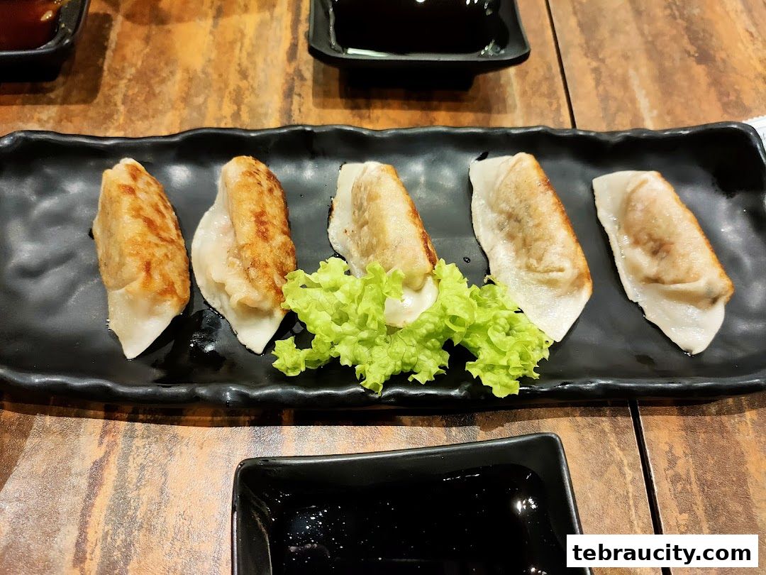 A plate of five pan-fried gyoza dumplings served with lettuce and dipping sauce.