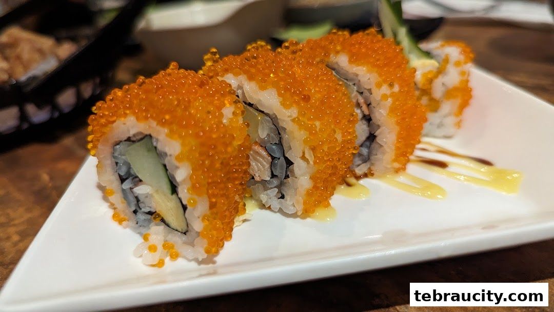 A close-up of California rolls covered in orange tobiko, served on a white plate with sauce.