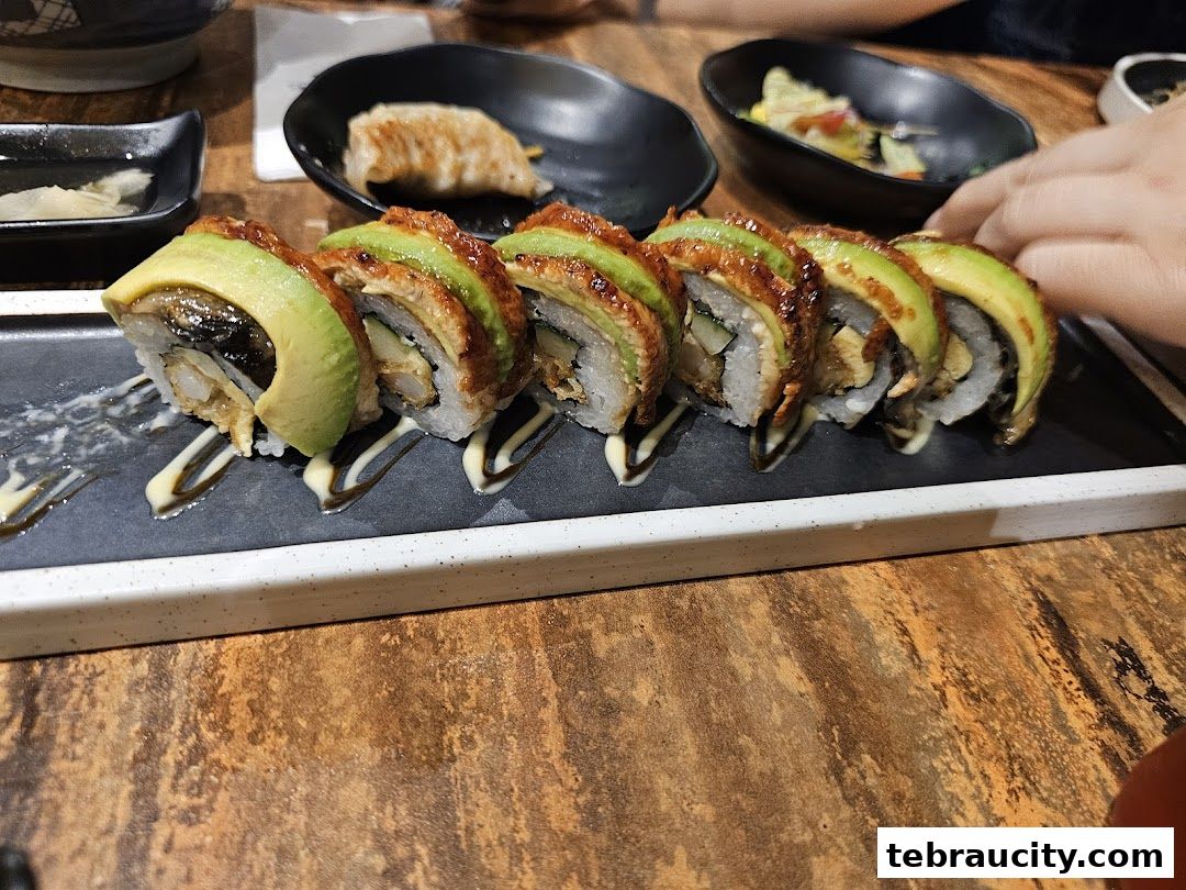 A close-up of a delicious sushi roll topped with avocado and eel, served with dipping sauce.