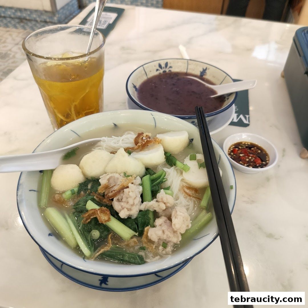 A bowl of noodle soup with fish balls, vegetables, and a side of red bean soup and iced tea.