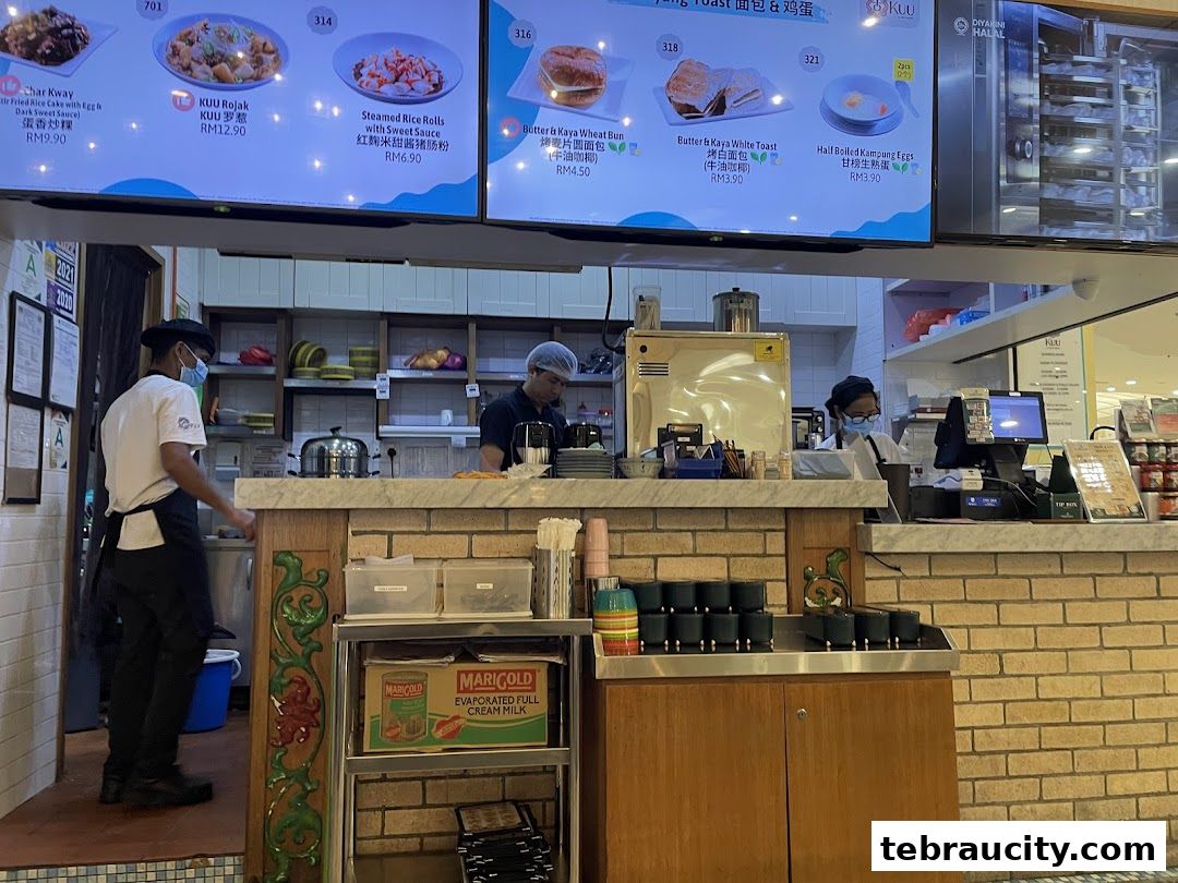 Staff preparing food behind a counter with a digital menu board displaying food items.