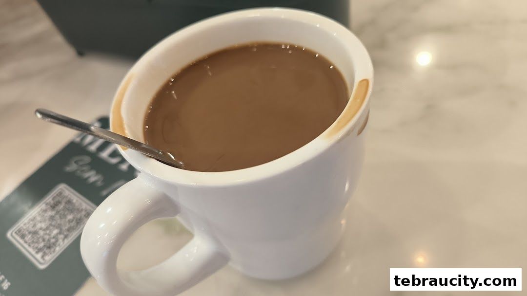 A close-up shot of a white mug filled with a milky coffee, with a spoon resting inside.