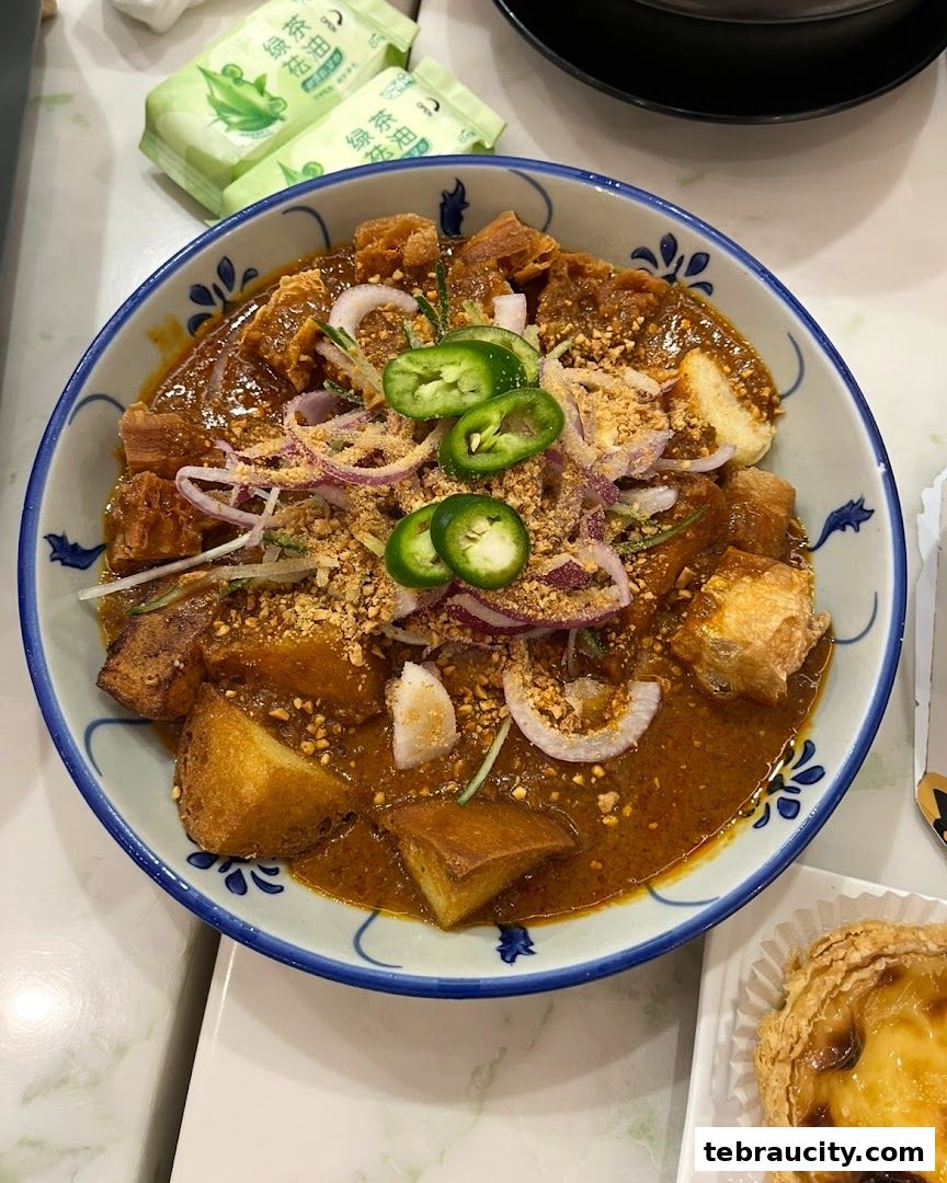 A bowl of curry noodles with toppings and an egg tart on the side.