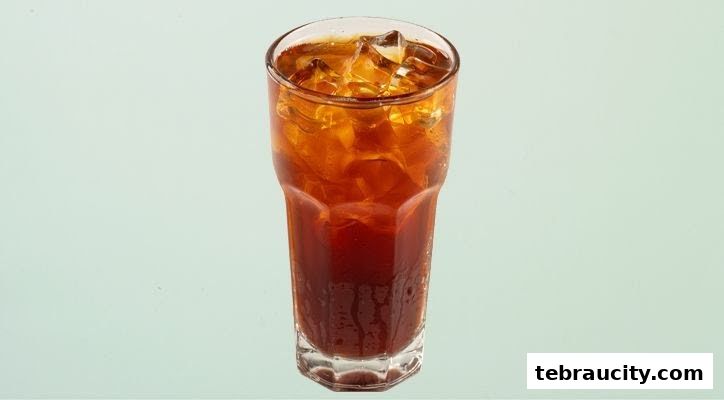 A tall glass filled with iced tea and ice cubes against a light blue background.