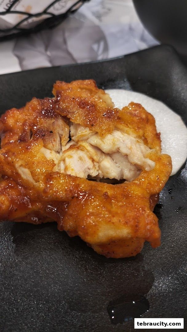A close-up shot of a piece of crispy, glazed fried chicken on a black plate.