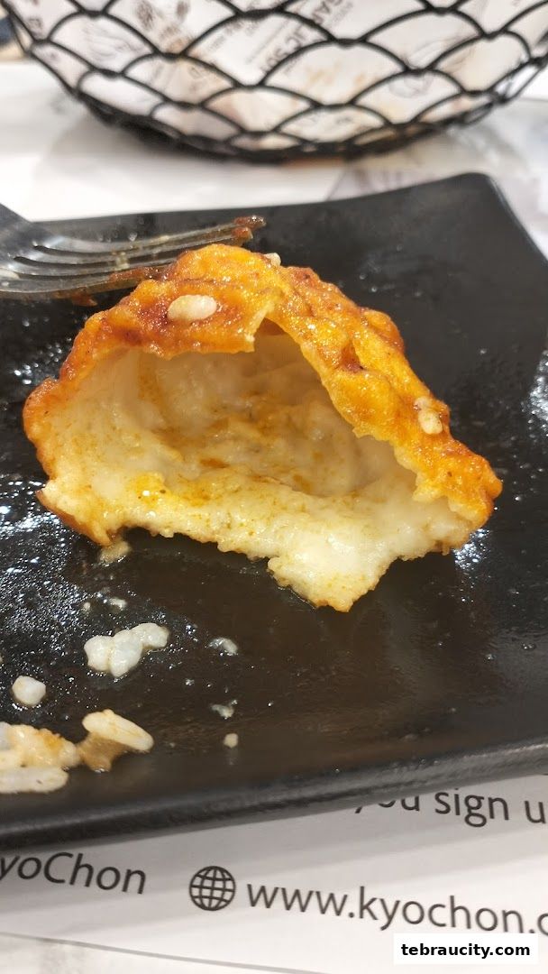 A close-up of a half-eaten Korean fried chicken piece on a black plate.