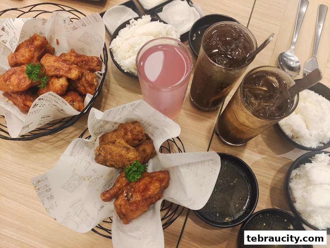 A table laden with Korean fried chicken, rice, drinks, and dipping sauces.