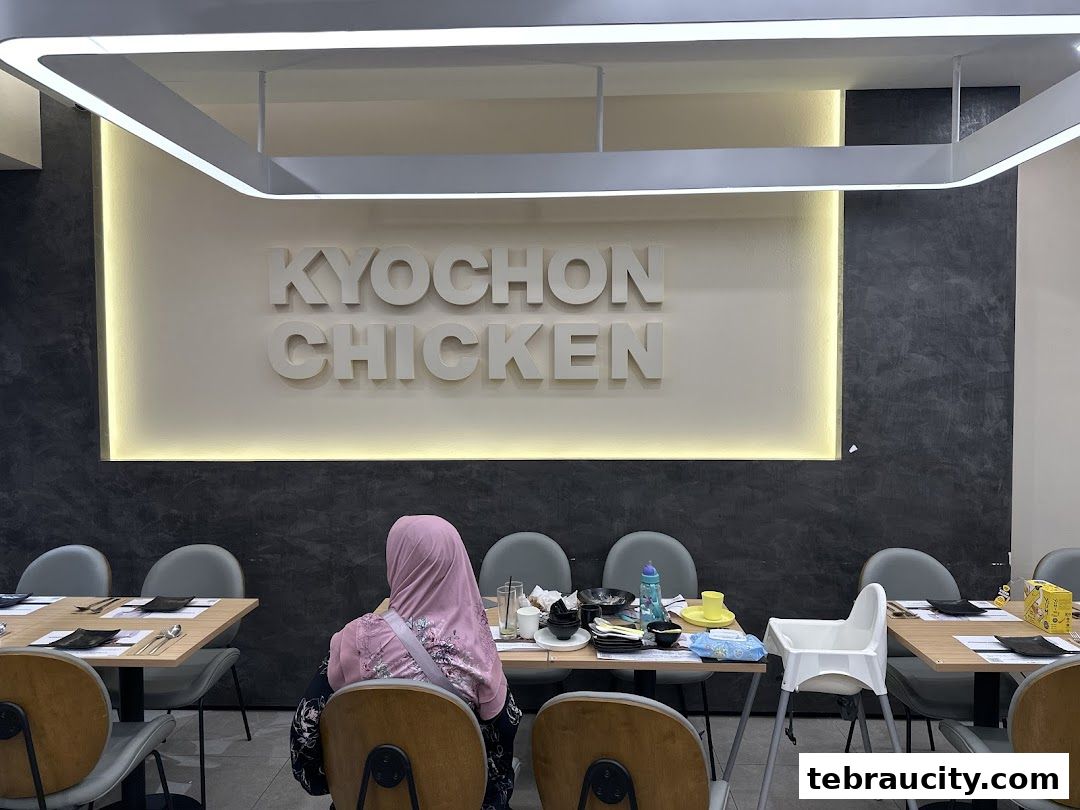 Interior of KyoChon Chicken restaurant with tables, chairs, and the restaurant logo on the wall.
