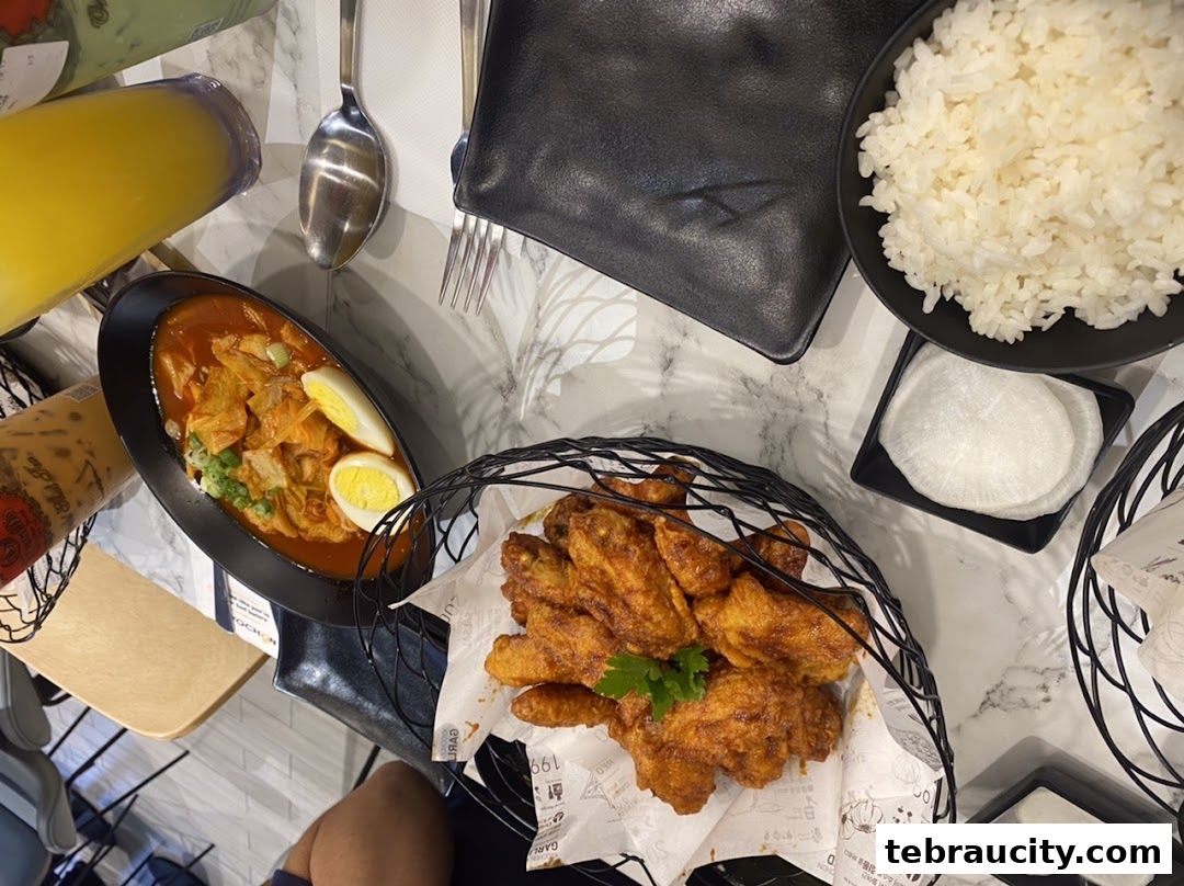 A table spread with Korean fried chicken, tteokbokki, rice, and drinks.