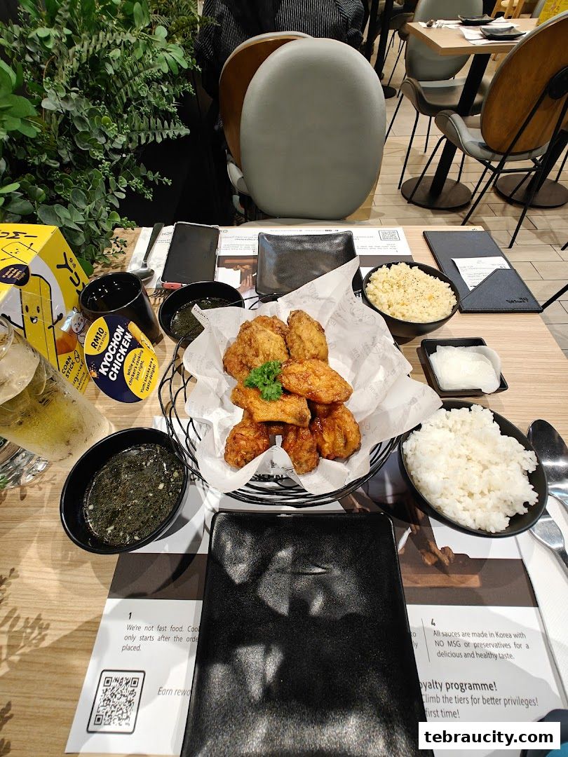 A table setting with KyoChon fried chicken, rice, dipping sauce, and a drink.