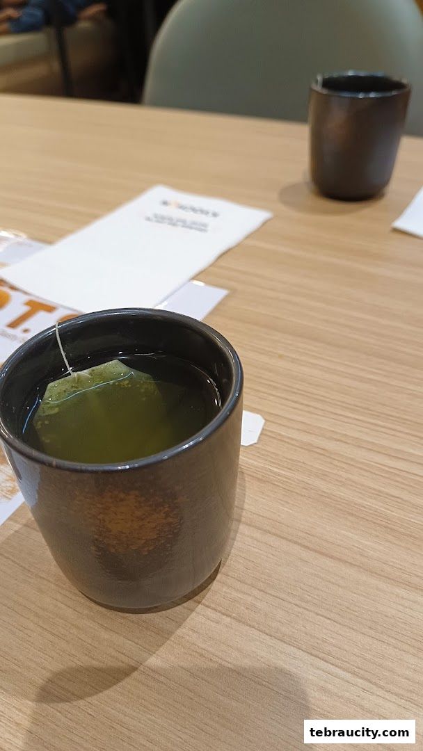 A close-up of a cup of green tea with a tea bag in a dark ceramic mug.