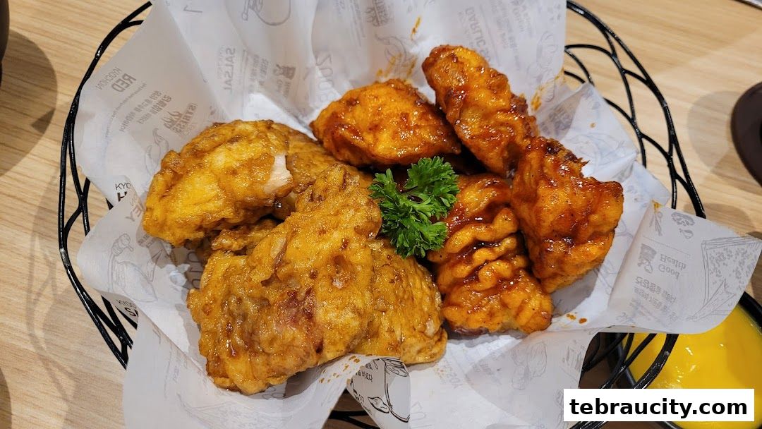 A basket of crispy fried chicken pieces, some coated in sauce, served with a side of yellow dipping sauce.