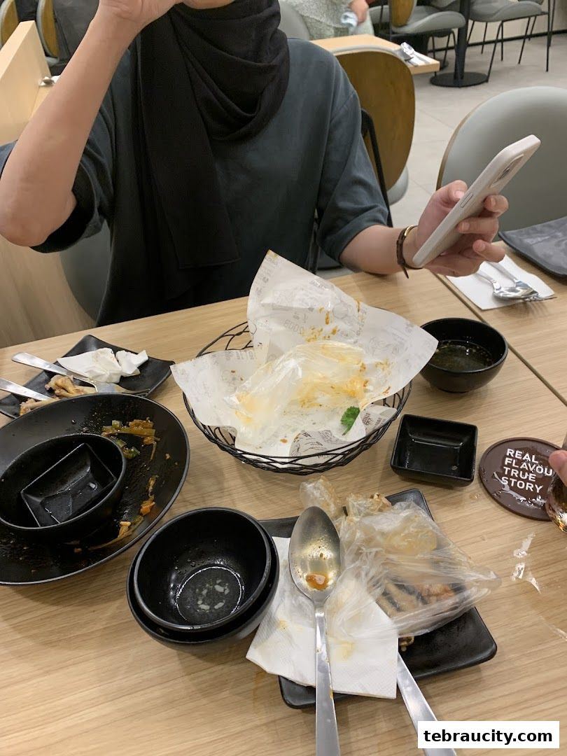 A table with leftover food and dishes after a meal, with a person holding a phone.