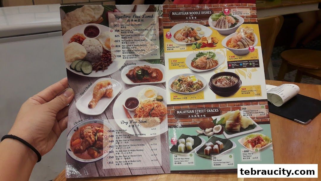A person holds a menu featuring Malaysian dishes like Nasi Lemak, noodle dishes, and street snacks.