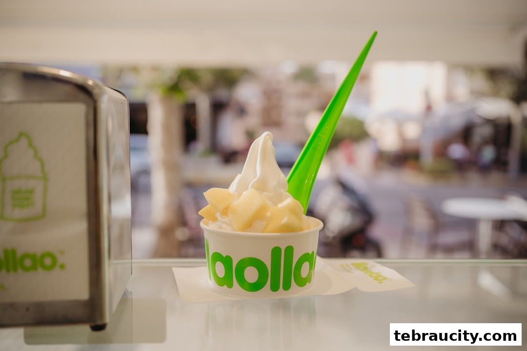A cup of frozen yogurt with fruit toppings and a green spoon from Llaollao.