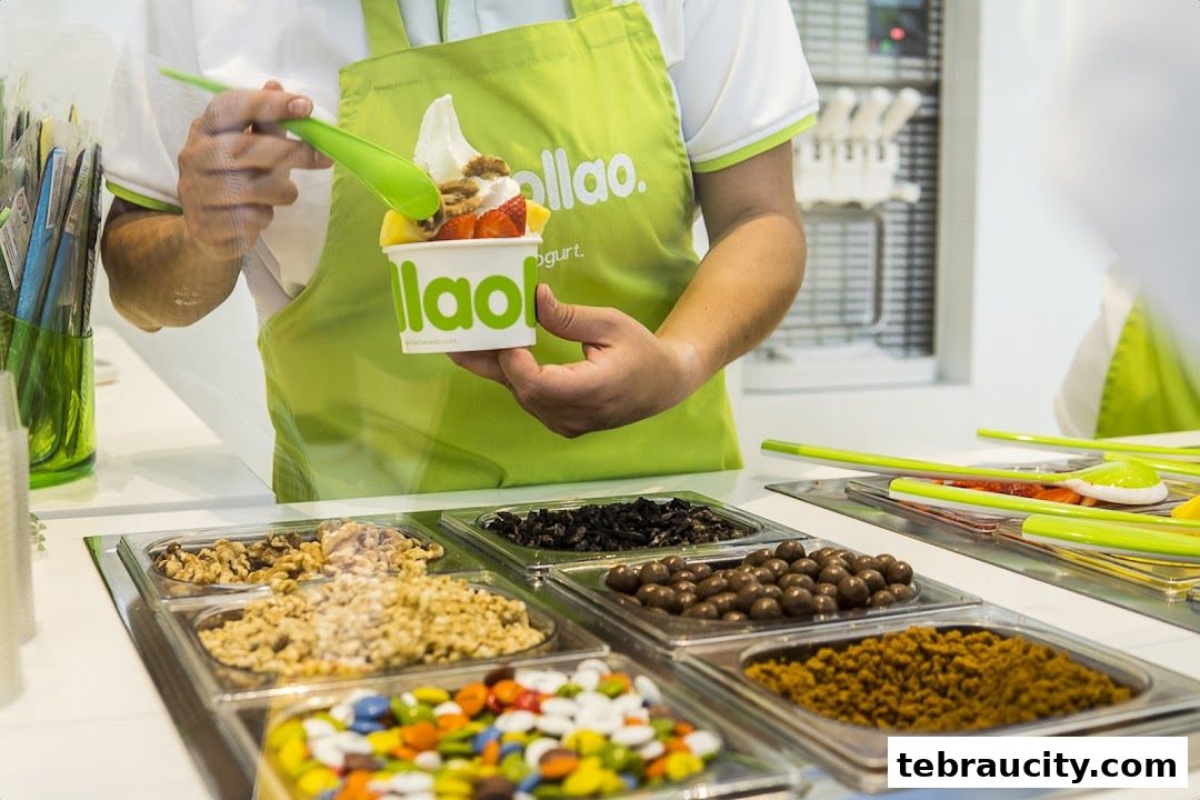 A person is preparing a frozen yogurt cup with fruits and toppings at Llaollao.