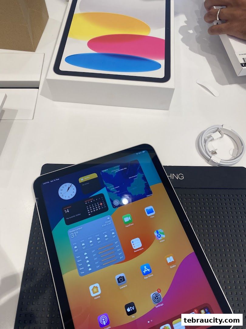 An iPad and its box are displayed on a white surface, with a charging cable nearby.