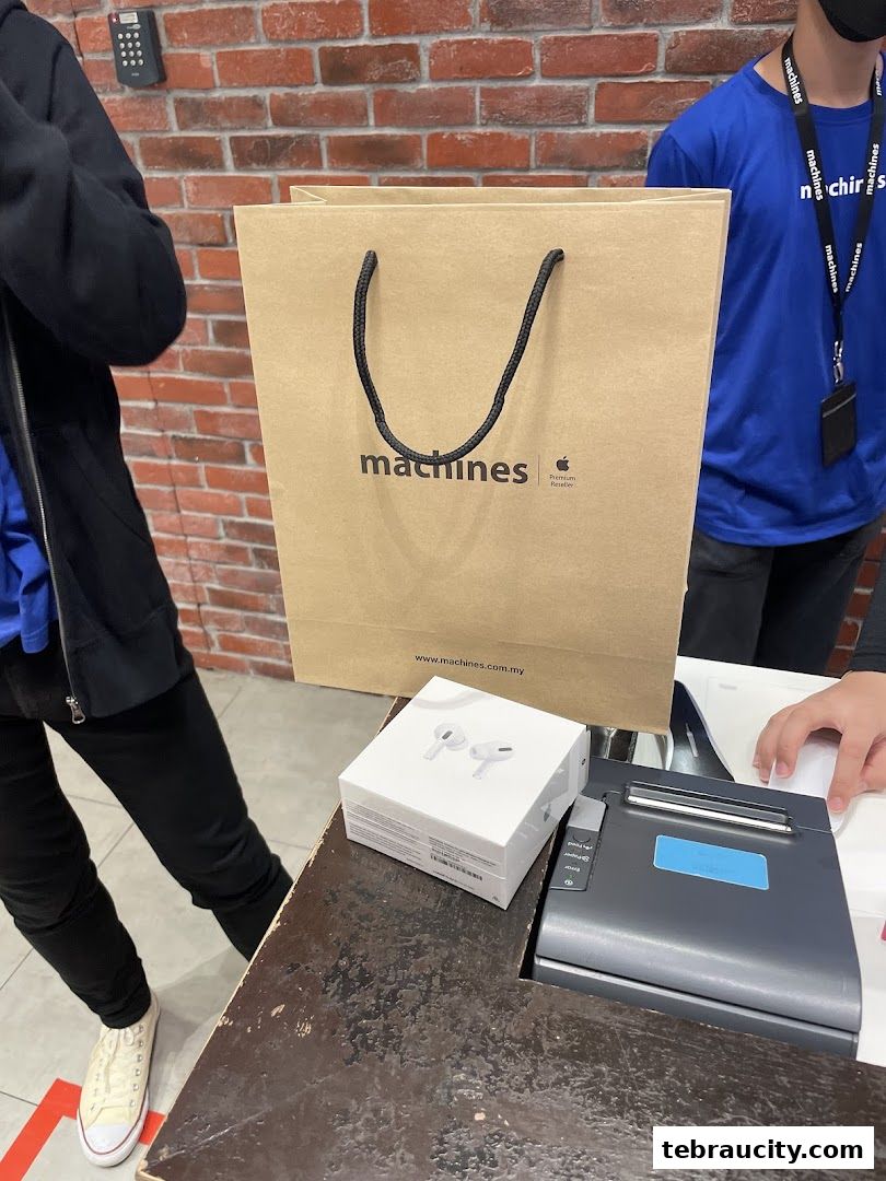 A customer receives a shopping bag and AirPods Pro box at a Machines Apple Reseller Store.