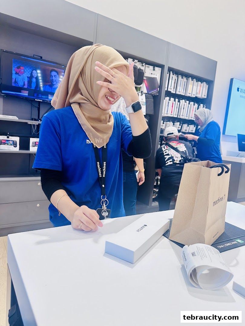 A smiling employee in a blue shirt and hijab at a counter with an Apple Watch box.