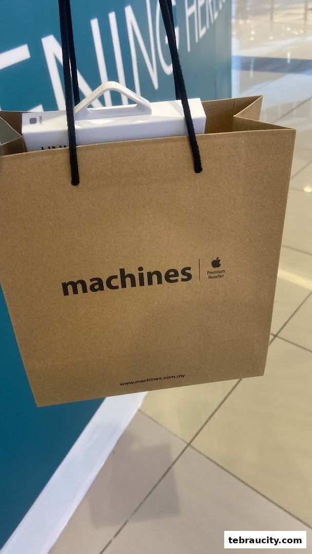 A brown paper shopping bag with the Machines Apple Premium Reseller logo and a white Apple product inside.
