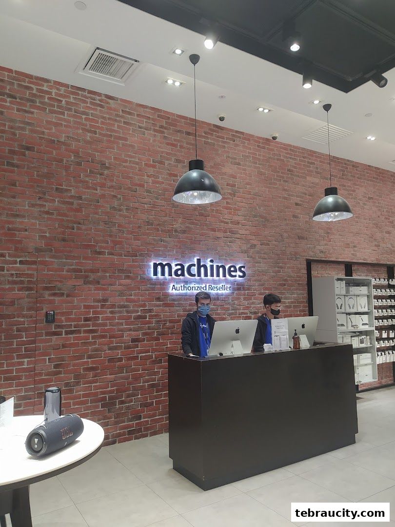 Two staff members stand behind a counter at an Apple Reseller store with a brick wall background.
