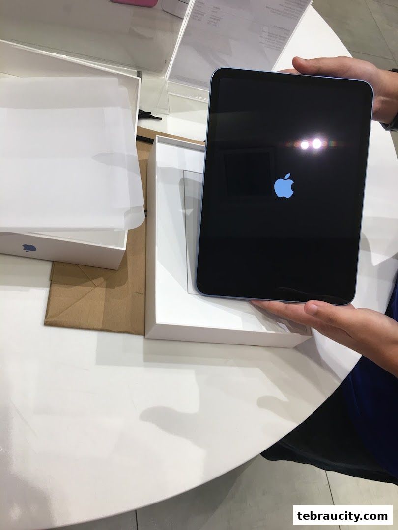 A person holds a new blue iPad with the Apple logo displayed on its screen.