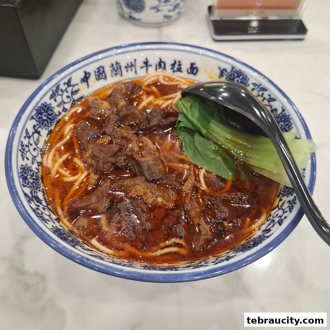 A close-up of a steaming bowl of beef noodle soup with bok choy and a spoon.