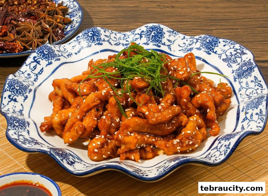 A plate of crispy, glazed meat with sesame seeds and green onions, served with a side of dipping sauce.