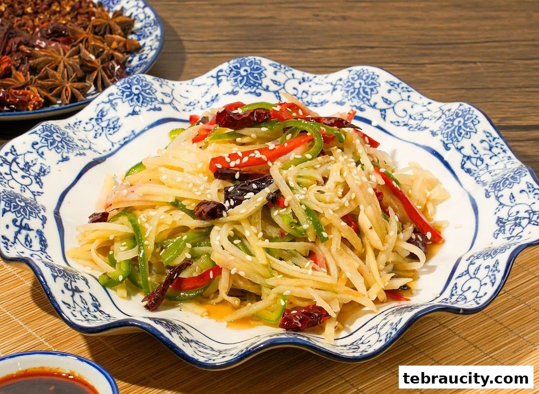 A plate of shredded potato salad with peppers and chili, garnished with sesame seeds.