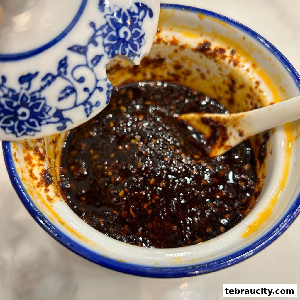 A close-up of a bowl of chili oil with a spoon and a decorative lid.