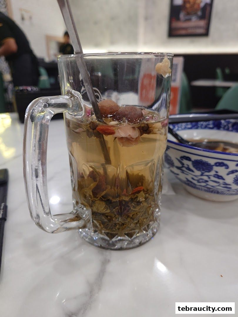 A glass mug filled with a herbal tea and dried fruits, with a bowl in the background.
