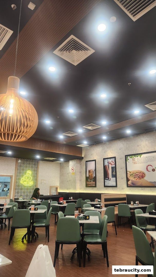 Interior of a restaurant with green chairs and tables, modern lighting, and wall decor.