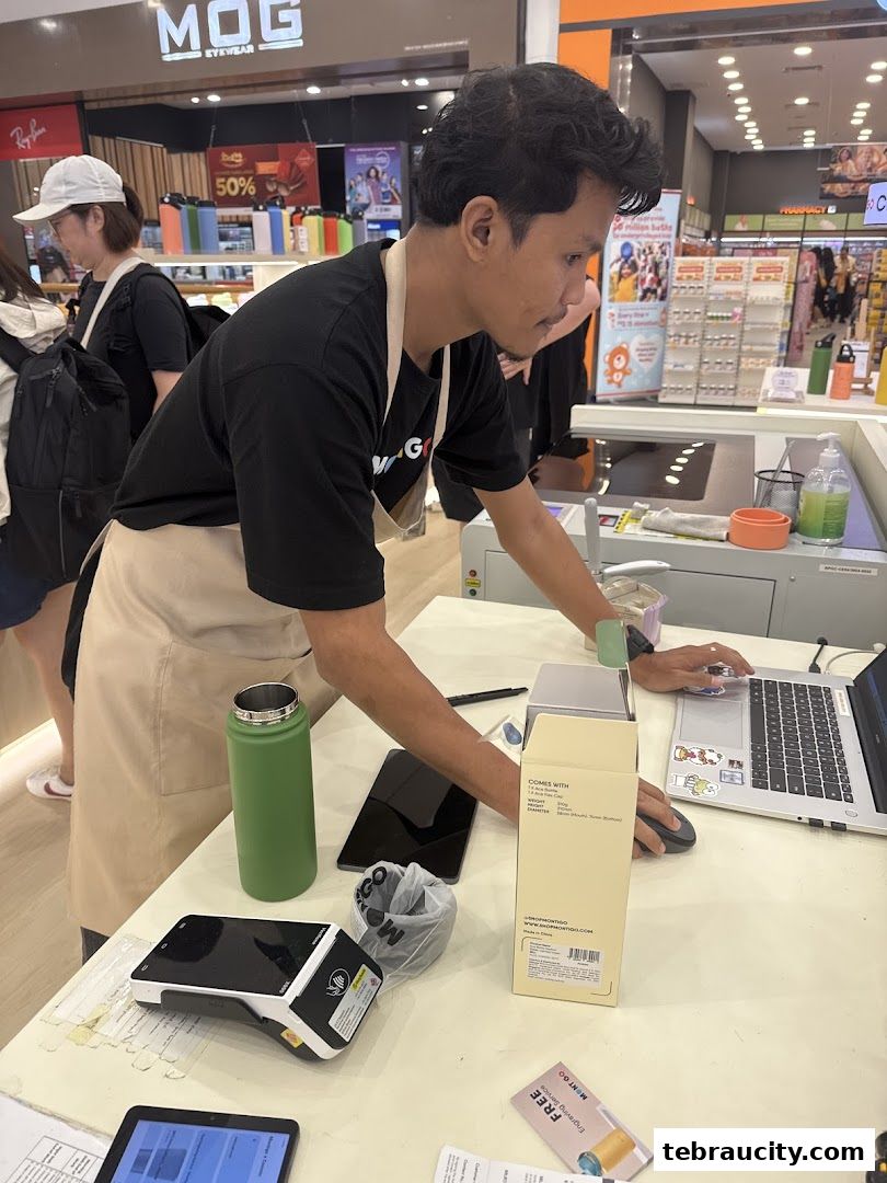 A shop assistant is using a laptop at a counter with various items on display.