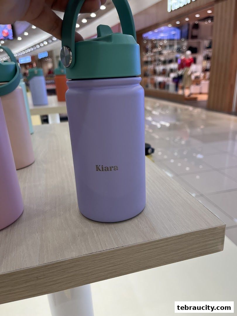 A close-up of a personalized purple water bottle with a green lid and handle.