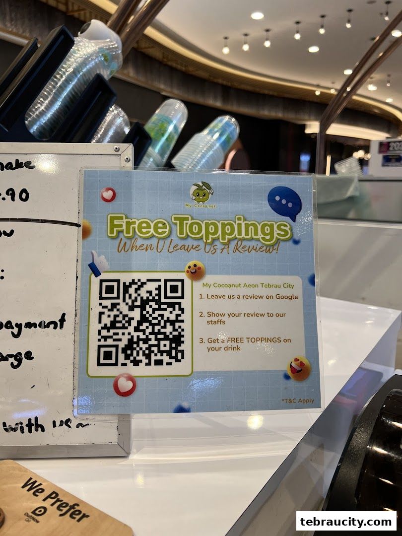 A sign offering free toppings for leaving a review at My Cocoanut Aeon Tebrau City.