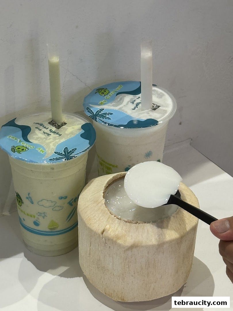 A hand scoops coconut flesh from a fresh coconut next to two refreshing coconut drinks.