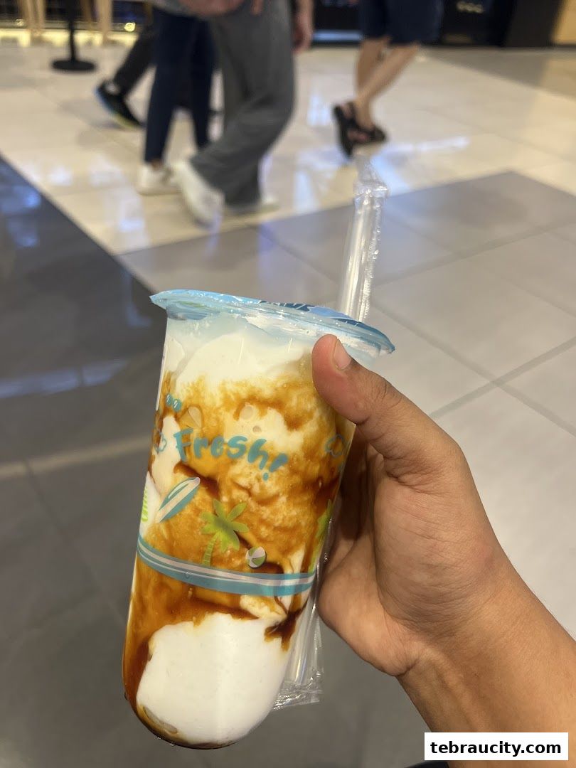 A hand holds a refreshing beverage with a caramel swirl and tropical graphics.