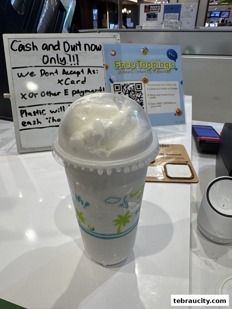 A refreshing coconut drink with a sign about payment methods and a promotion for free toppings.