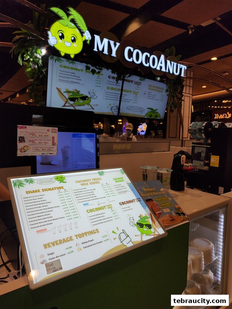 A brightly lit counter at My Cocoanut Aeon Tebrau City, showcasing a menu and fresh coconuts.