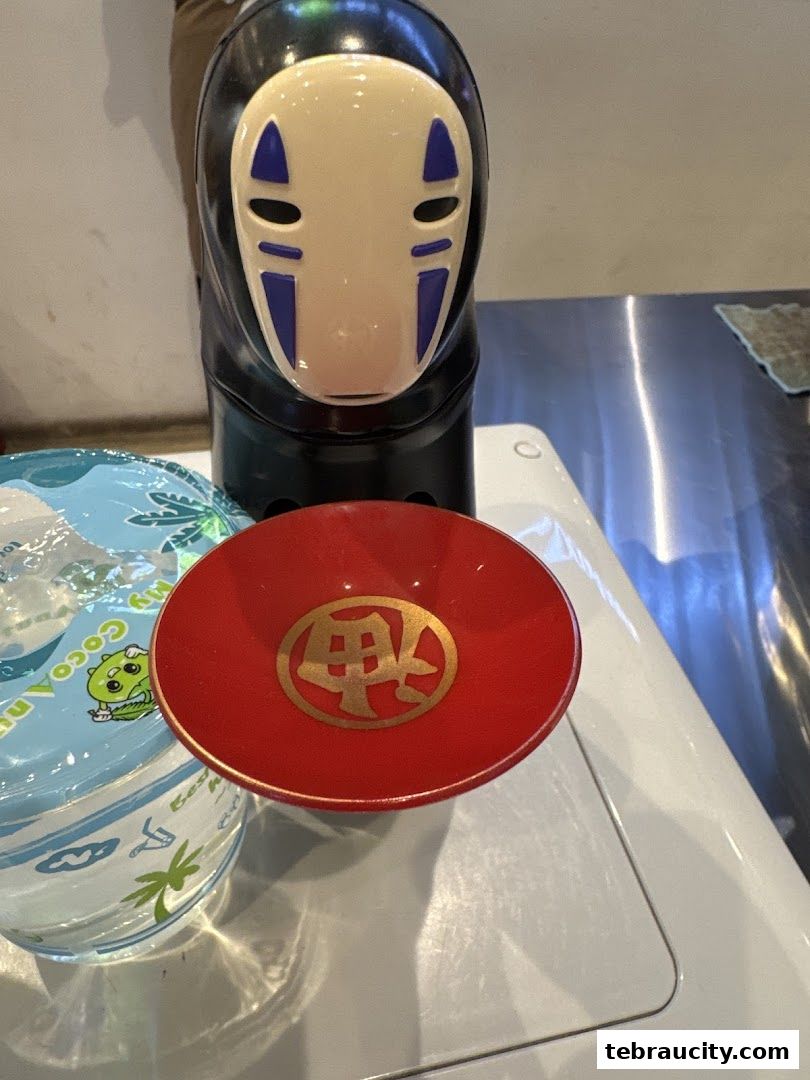 A close-up of a No-Face character figurine with a red sake cup.