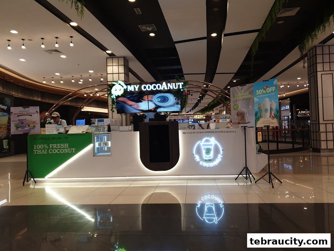 A brightly lit coconut drink stall with promotional posters and a neon sign.