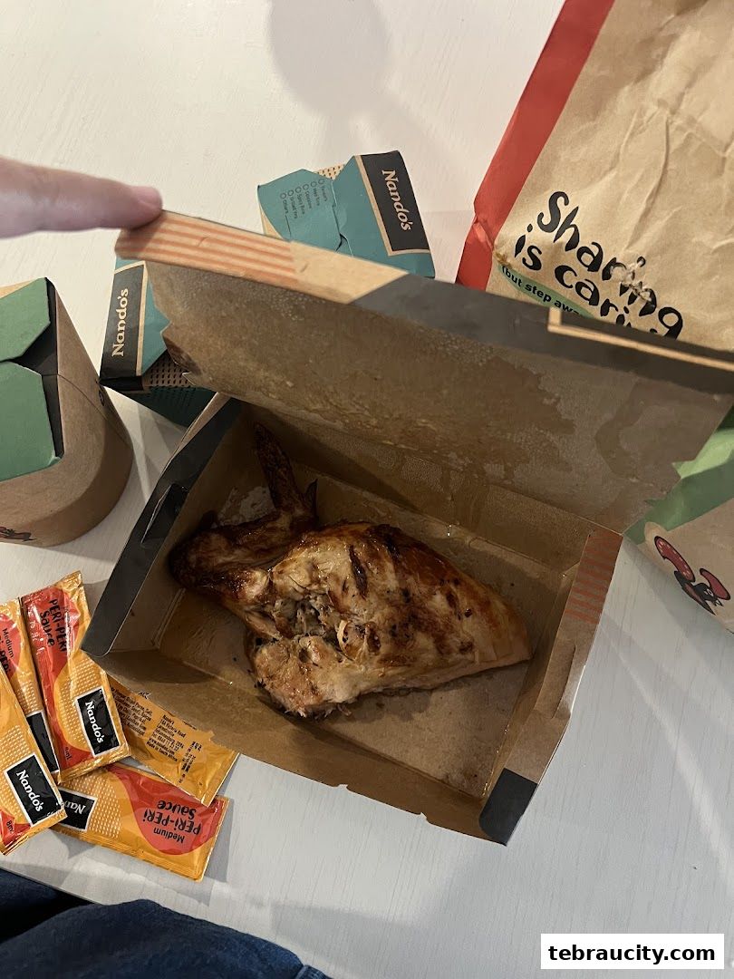 A half chicken meal from Nando's with peri-peri sauce packets and branded packaging.