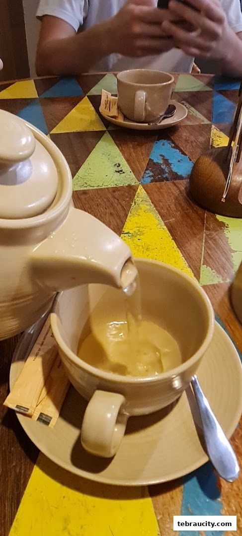 A teapot pours a beverage into a cup on a colorful, geometric-patterned table.