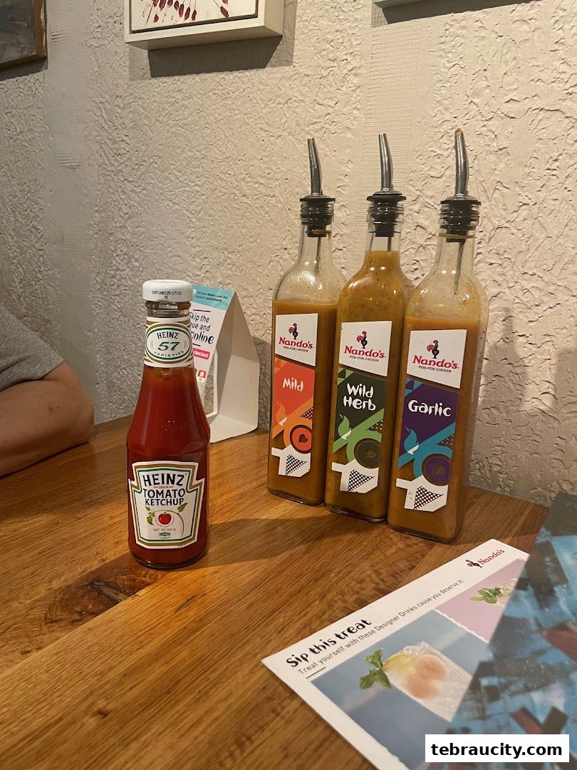 A bottle of Heinz ketchup and three bottles of Nando's sauces on a wooden table.