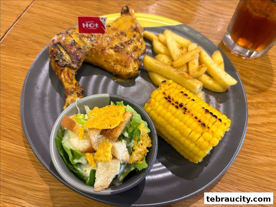 A plate of grilled chicken, fries, corn on the cob, and a side salad with a drink.